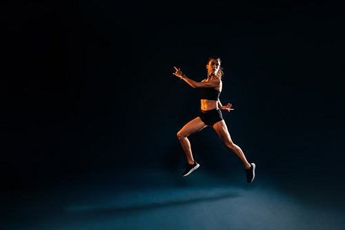 Runner in sports clothes jumping. Woman sprinting on black backg