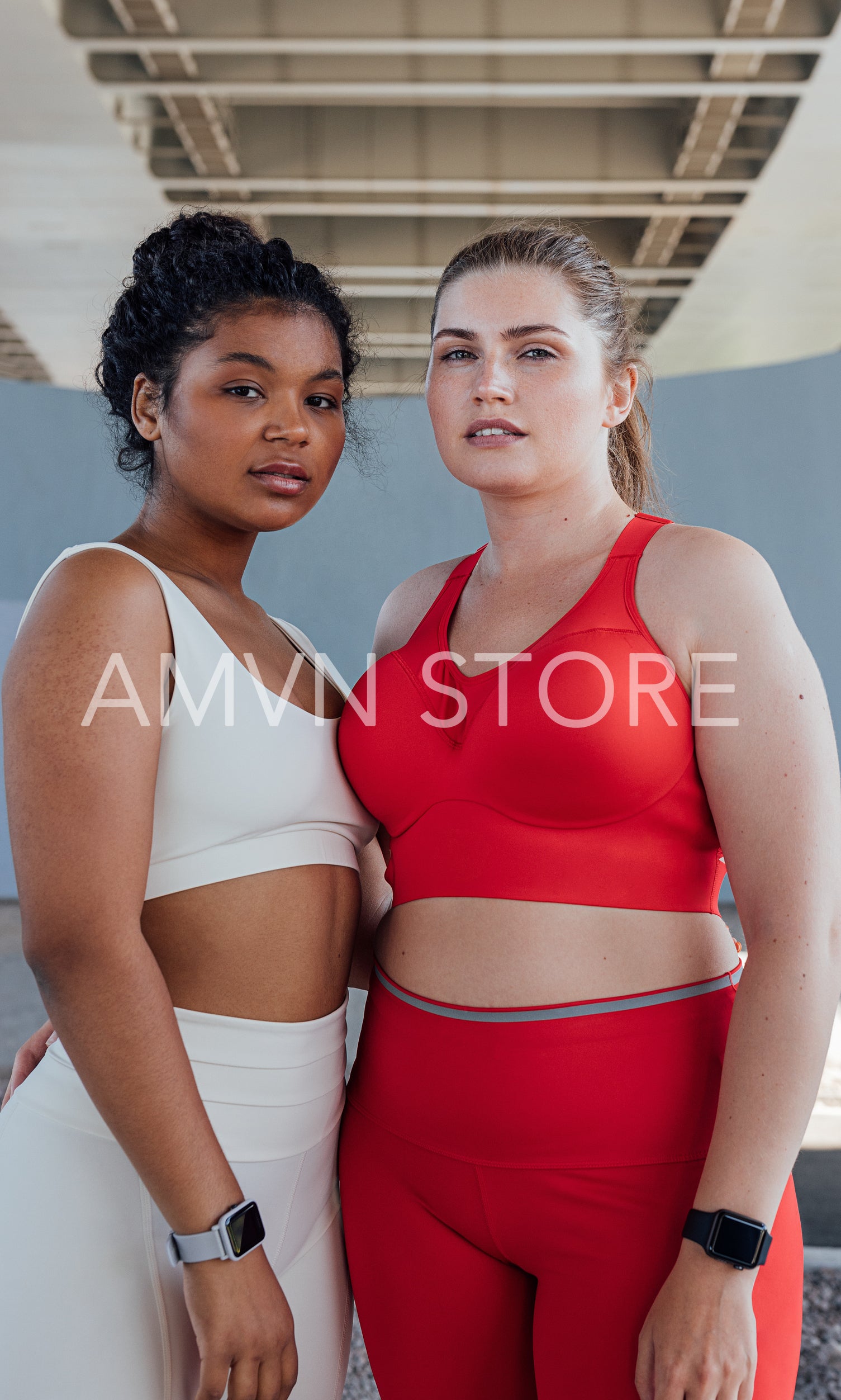 Portrait of two women in fitness attire with different colors looking at camera while standing outdoors