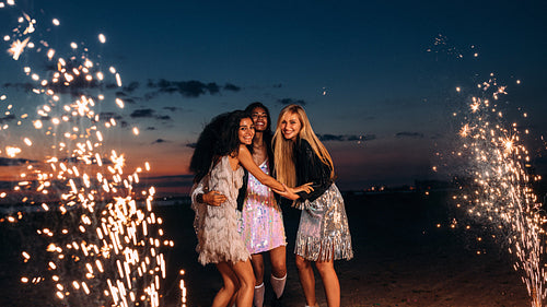 Four happy women celebrating with fireworks at sunset