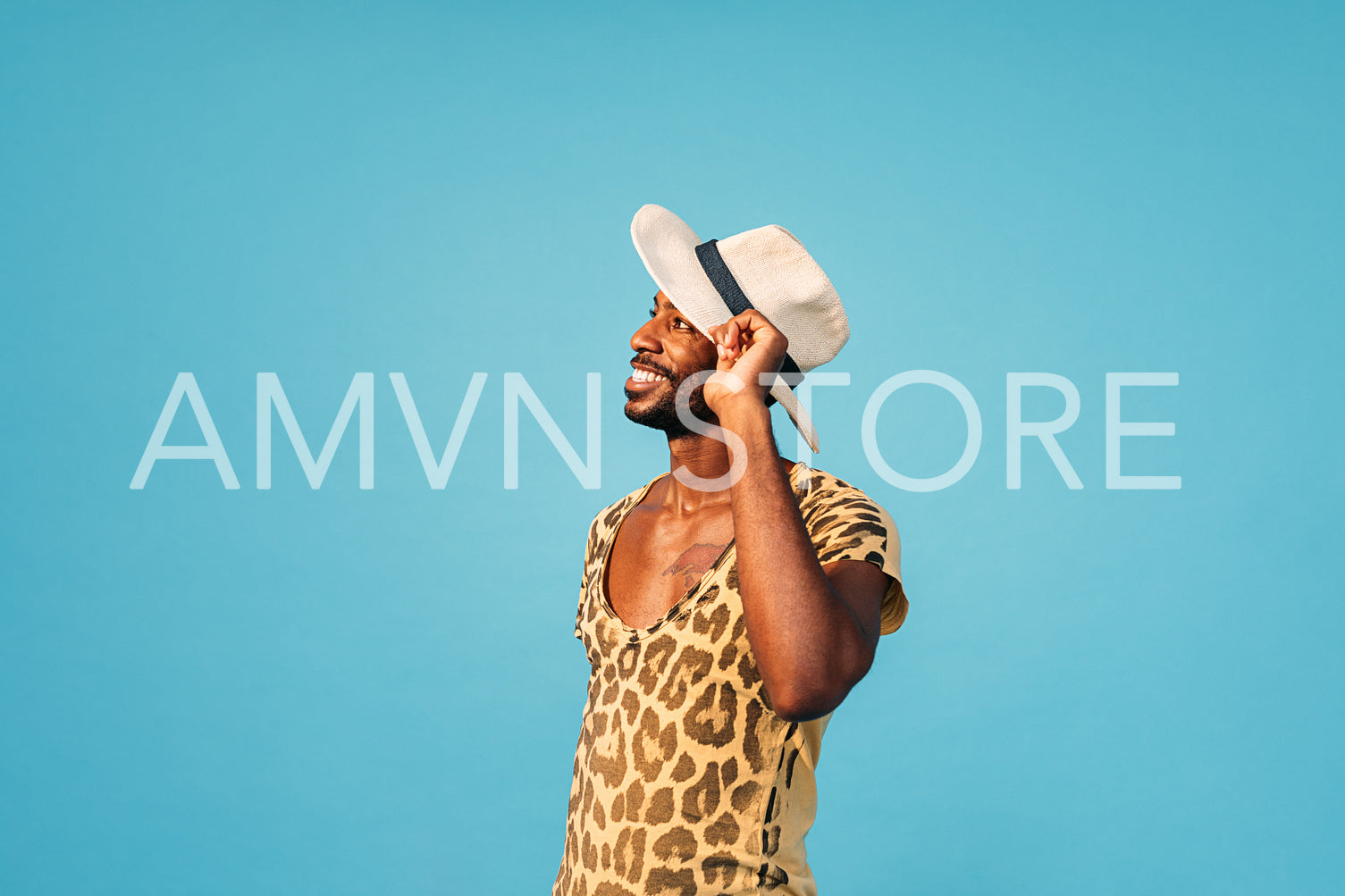 Young guy posing against a blue background. Stylish male with a straw hat.