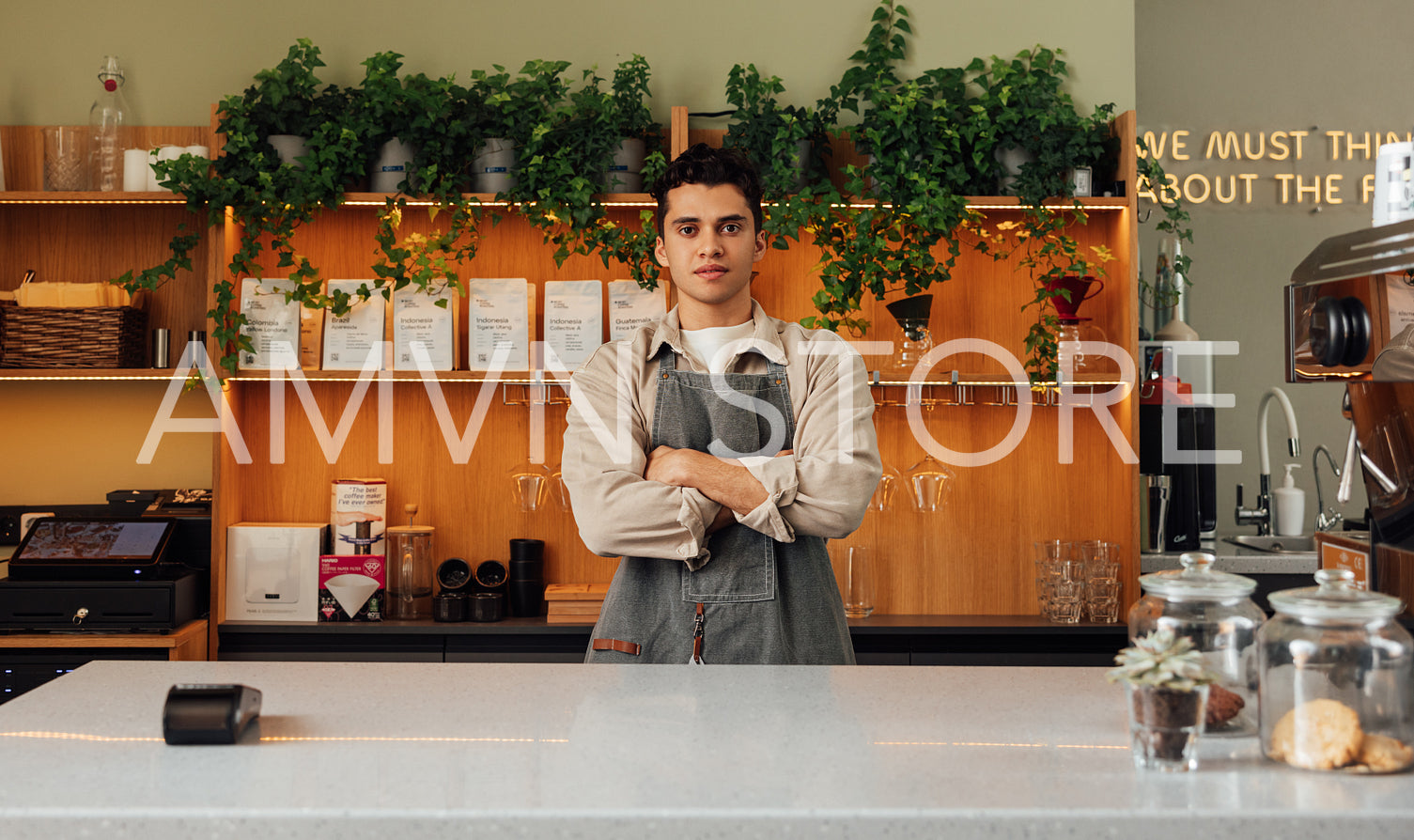 Young confident barista with cross hands looking straight at a camera while standing at a counter