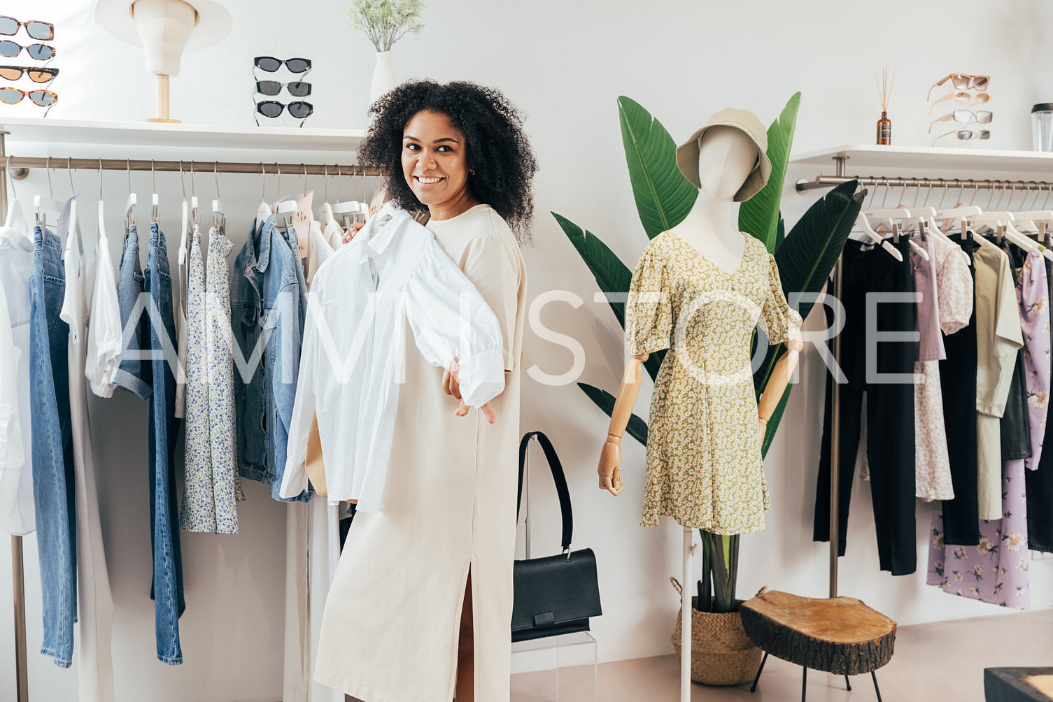 Cheerful woman trying on a shirt while standing at a rack in a small boutique