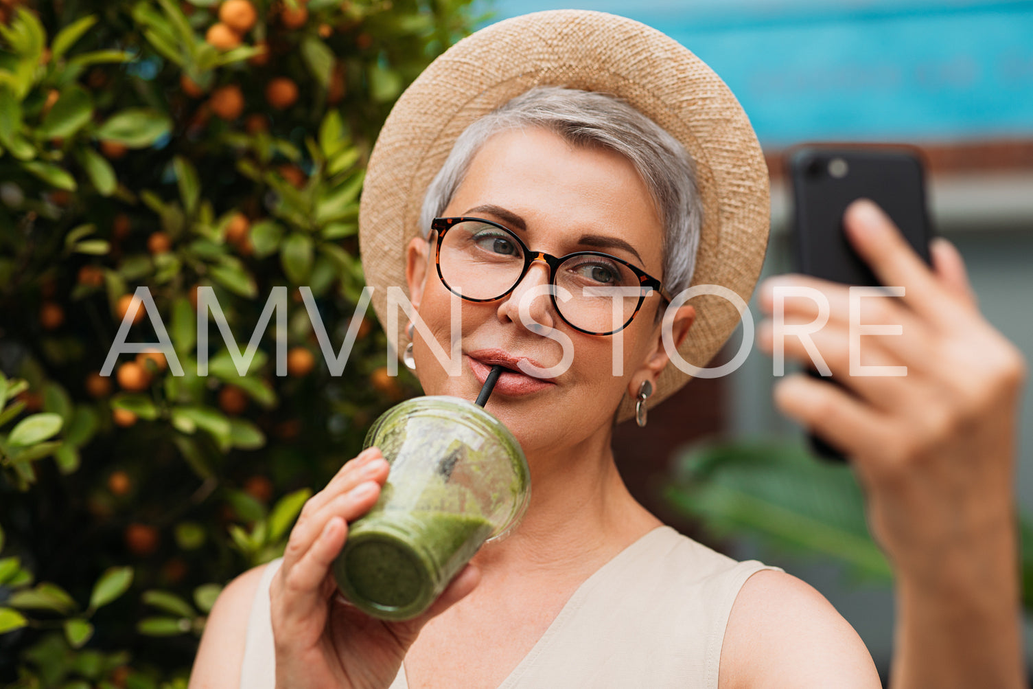 Stylish senior female drinking a smoothie and making selfie outdoors