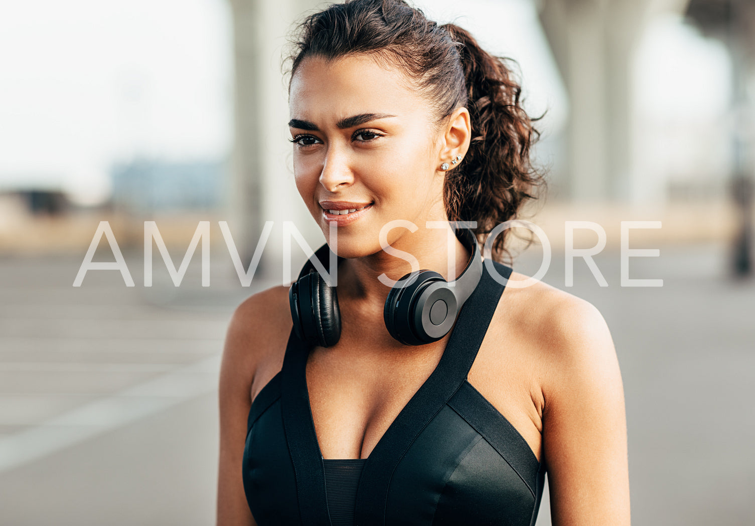 Portrait of a beautiful sportswoman with headphones on her neck. Smiling woman in sports bra standing outdoors.	