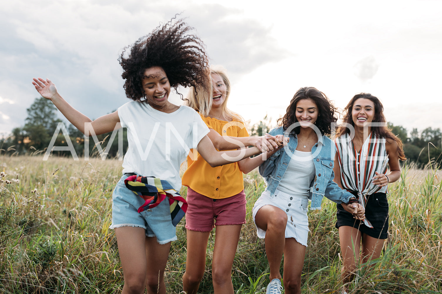 Four happy women hold hands and running on a field. Female friends having good times outdoors.