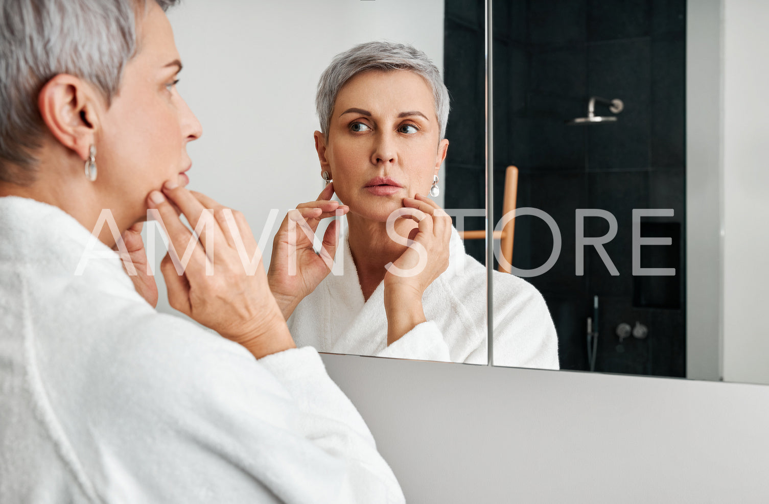 Mature woman with short grey hair wearing bathrobe standing in front of a bathroom mirror	