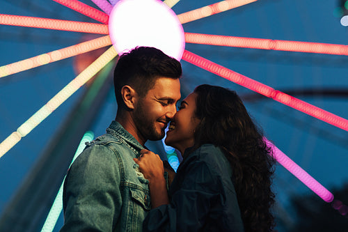 Side view of young happy couple against Ferris wheel at night