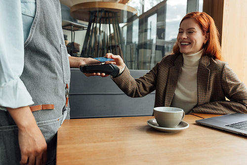 Happy woman paying for breakfast by card in coffee shop