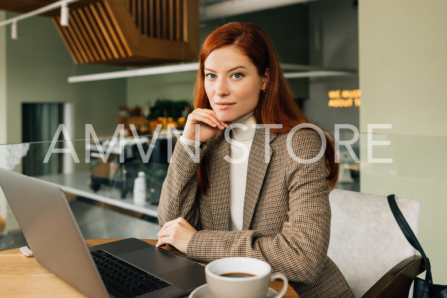 Portrait of a young businesswoman with ginger hair. Stylish female sitting at a table in a cafe with a laptop and coffee.