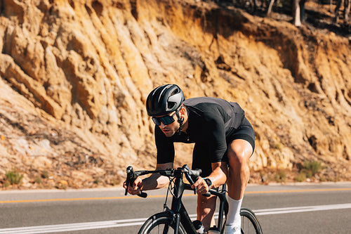 Tough cyclist on his road bike. Professional cyclist in black sport attire exercising in wild terrain.