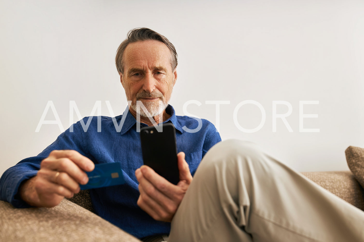 Senior man paying online. Male in casual clothes sitting on sofa holding a credit card