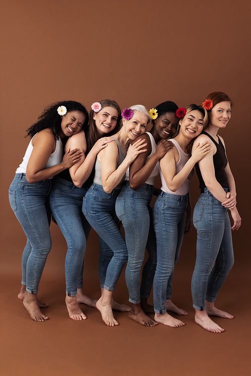 Full length of six women with flowers in their hair stands one after another against a brown background