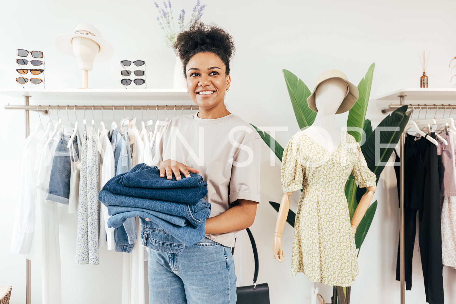 Smiling saleswoman standing in a small local store with a pile of jeans and looking away