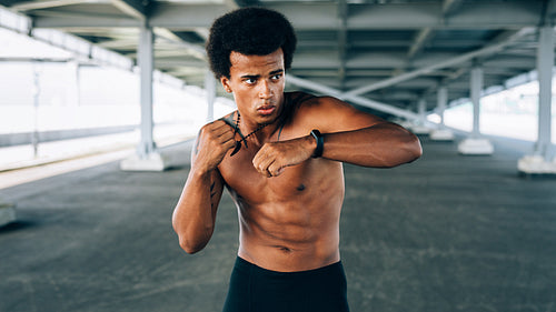 Young sportsman warming up under a bridge, doing boxing exercises