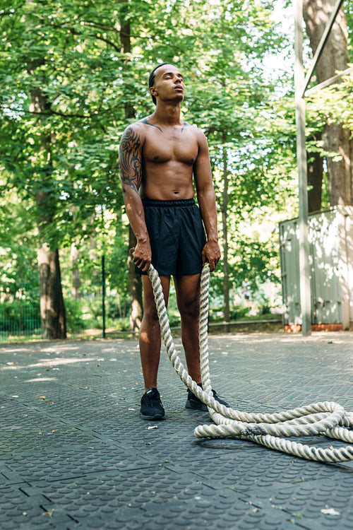 Fitness man standing holding two battle ropes during workout outdoors