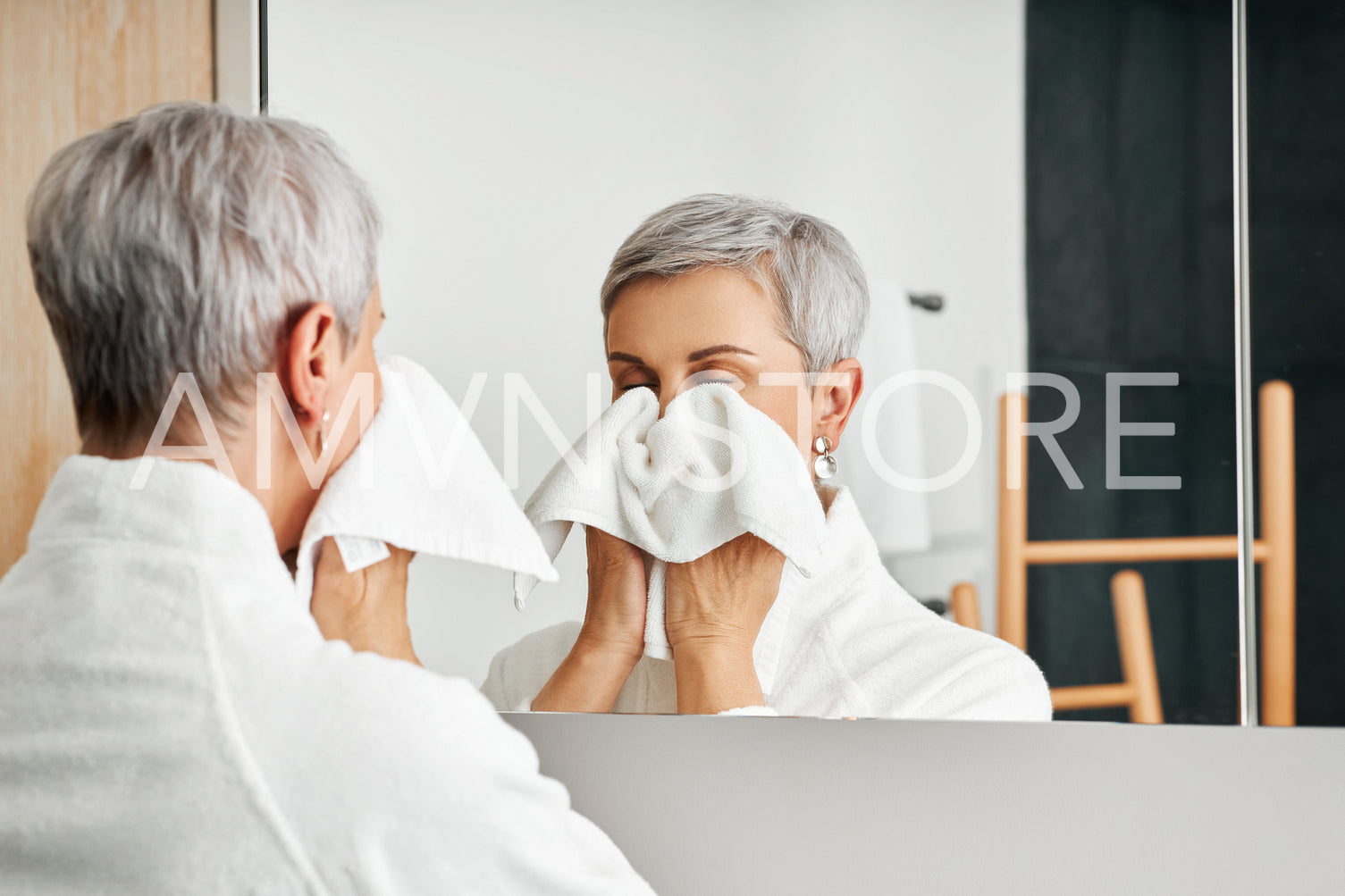 Senior woman wiping face with towel while standing in front of a mirror 