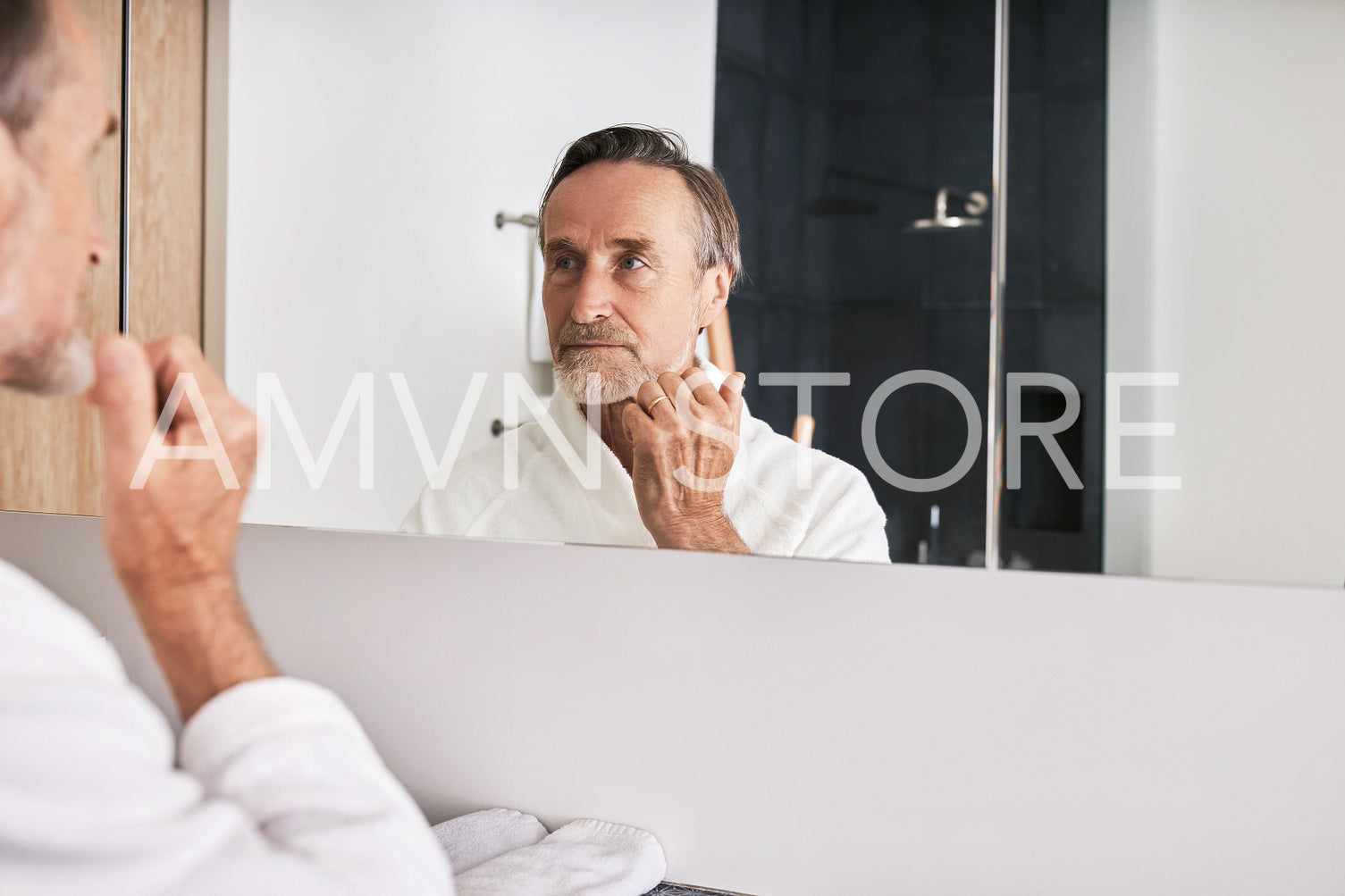 Handsome senior man wearing white bathrobe examine his skin in bathroom at morning	