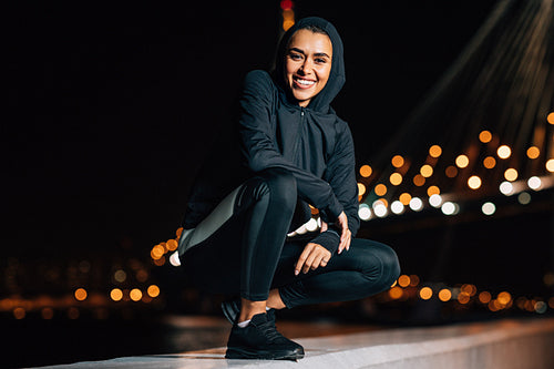 Cheerful middle east woman in sport hoodie shirt sitting outdoors at night looking at camera