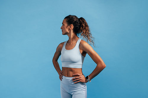 Side view of fitness female with hands on her waist standing on blue background