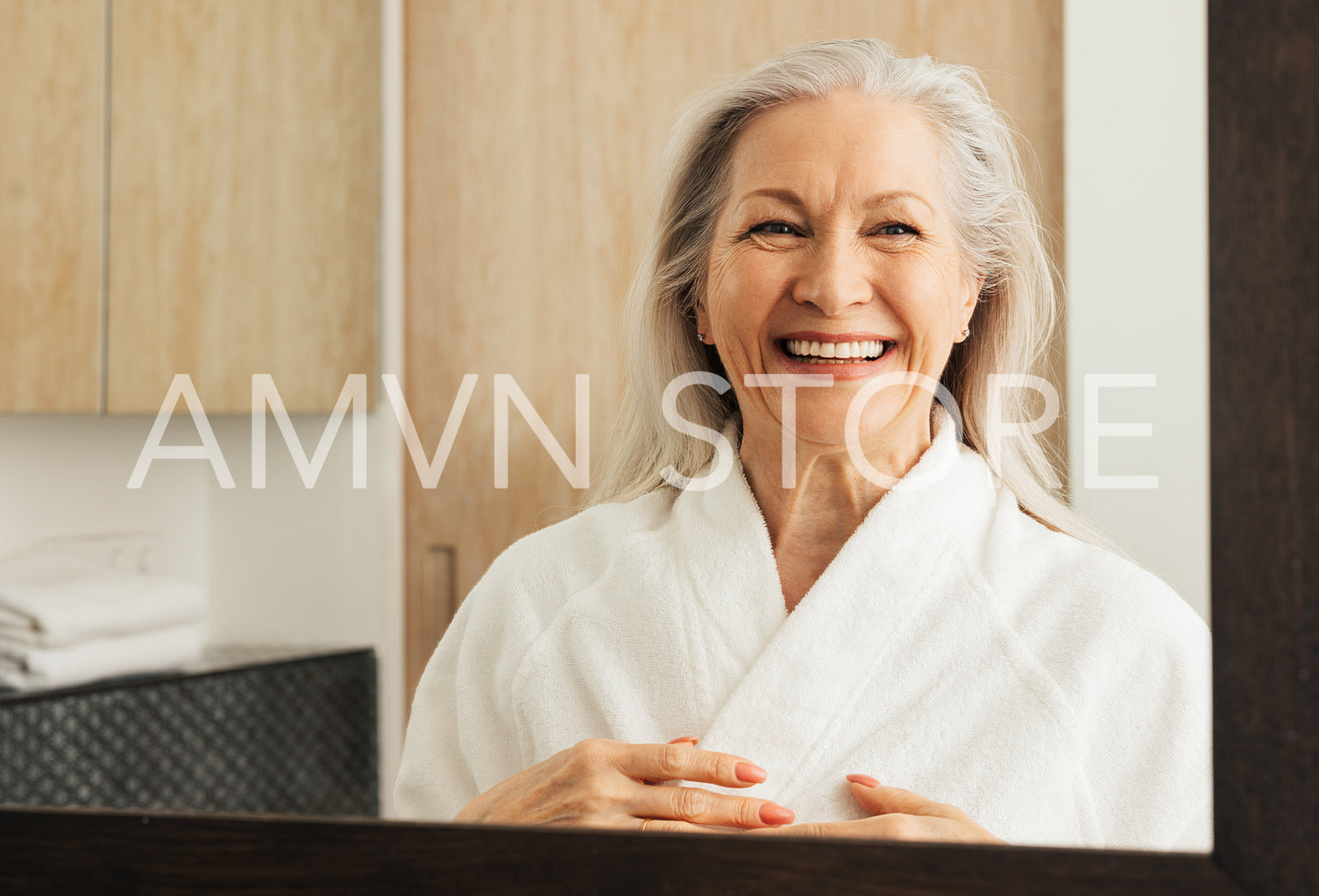 Laughing aged woman in a bathrobe in front of a mirror in the bathroom