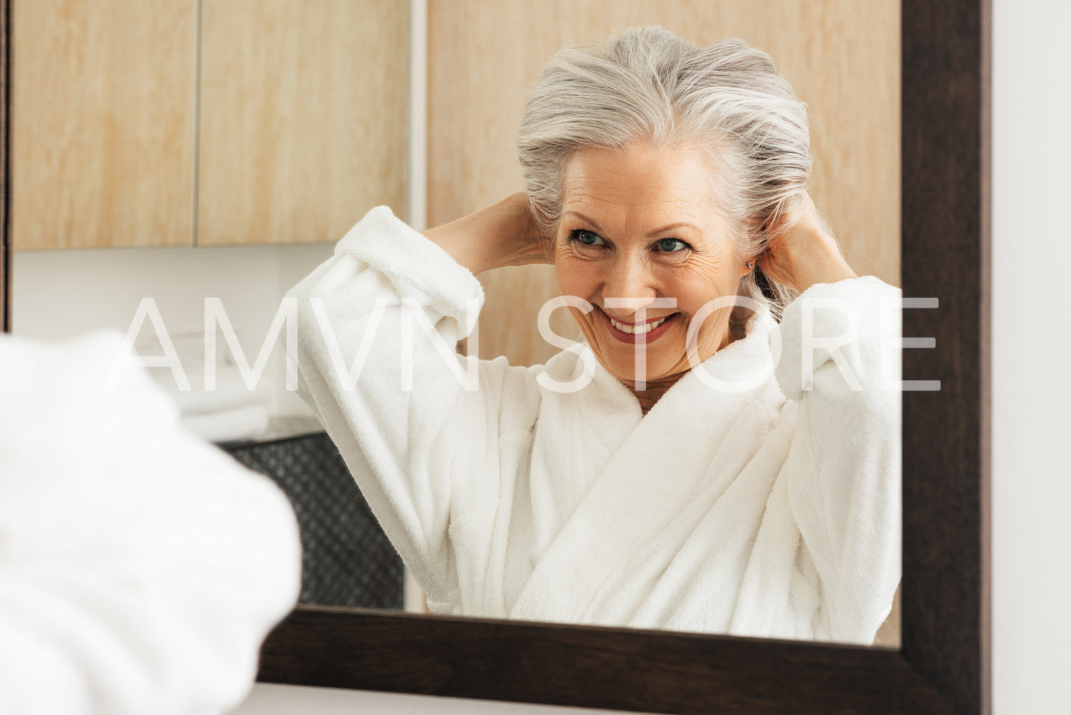 Smiling aged woman making funny hairstyle while looking at a mirror in bathroom. Senior female enjoying morning routine in the bathroom.