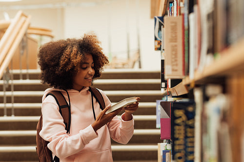 Smiling girl with curly hair holding a book near bookshelf in school library