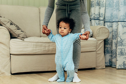 Toddler holding mother's hands in living room. Unrecognizable woman with son.