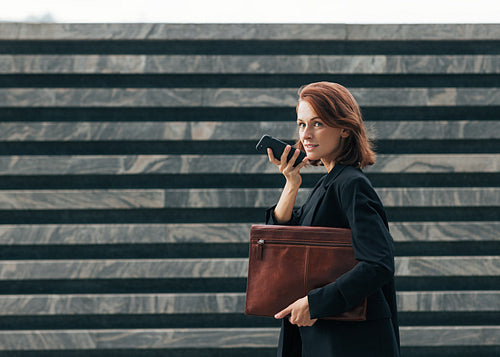 Side view of a middle-aged businesswoman recording a voice message on the go