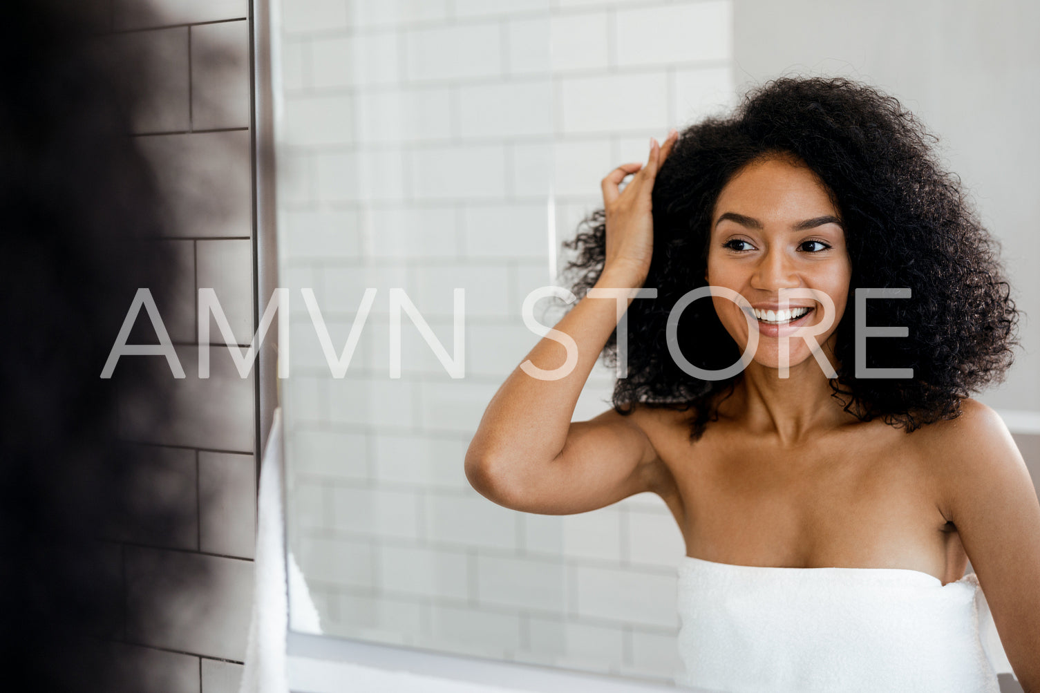 Young smiling woman examining her hair in the bathroom, looking into a mirror	