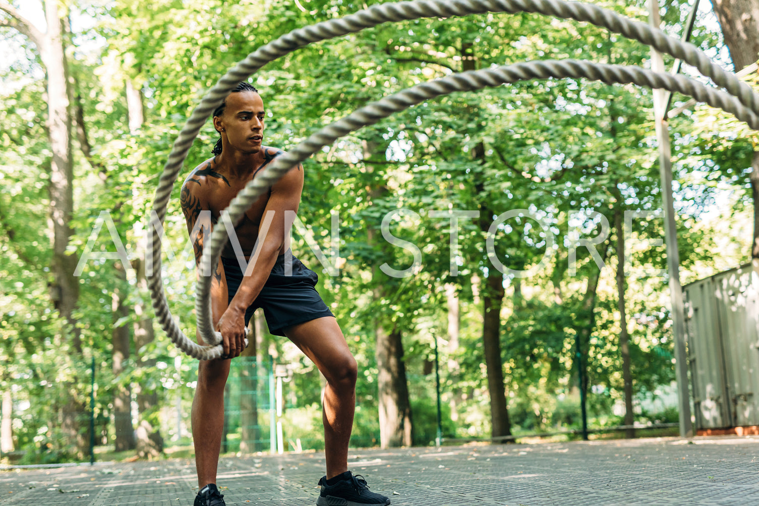 Bare chested muscular man doing workout using two battle ropes on sports ground	