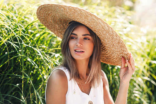 Portrait of a young woman in straw hat sitting in a park