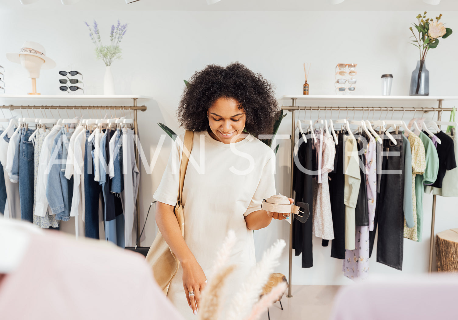 Stylish woman in boutique choosing belt. Young female standing in a local clothing store looking for accessories.