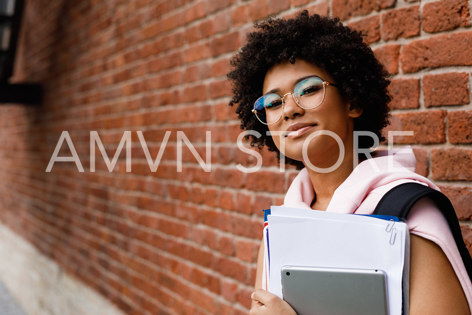 Teenage girl in glasses standing with books outdoors at wall	