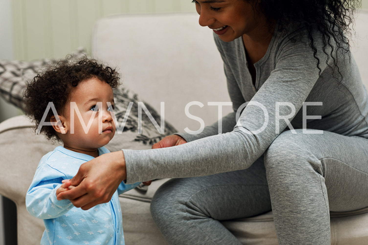 Young mother holding her child hands in living room. Toddler looking at camera.	