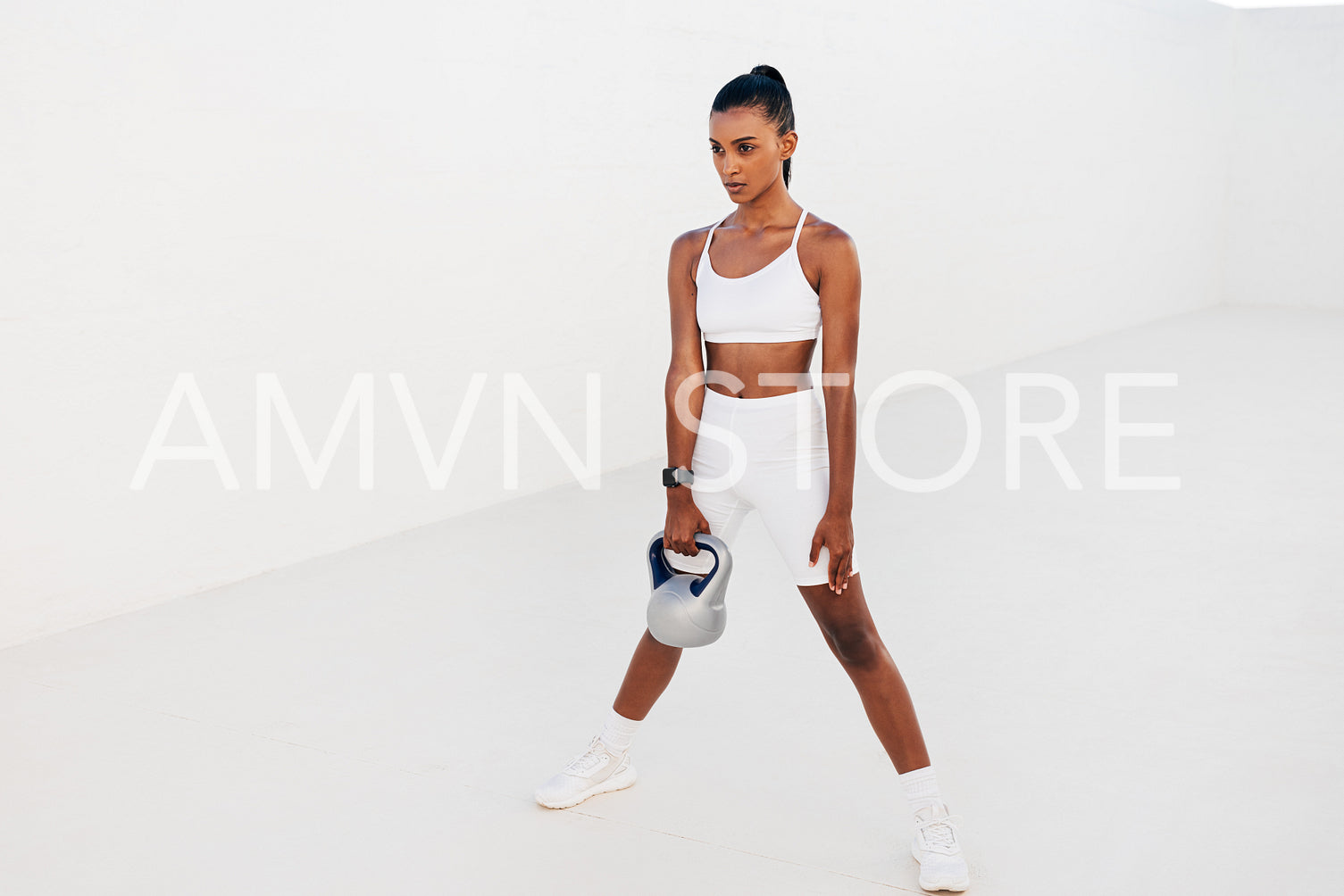 Woman standing with kettlebell outdoors. Female athlete exercising with weight in white outdoor studio.