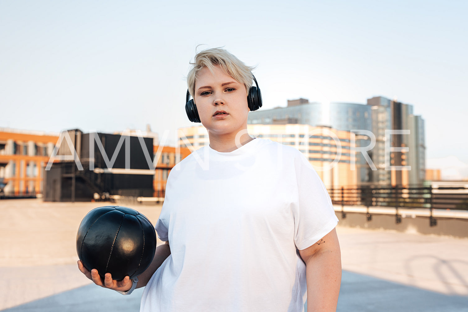 Confident female standing on the roof with medicine ball and headphones on her head	