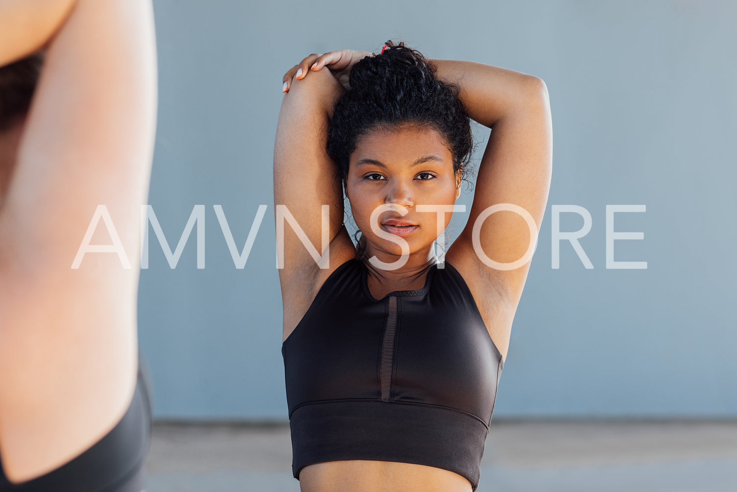 Young woman in black sportswear with curly hair warming up her hand and looking at camera 