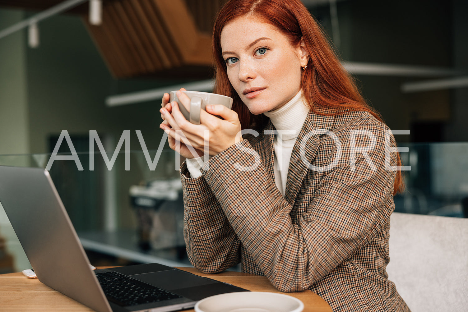 Portrait of a beautiful businesswoman with ginger hair holding a cup and looking at the camera while sitting in a cafe