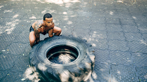 Muscular man doing squats with huge tire on sports ground outdoors