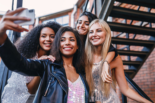 Group of stylish women taking selfie in the city. Four women making photographs on a cell phone.