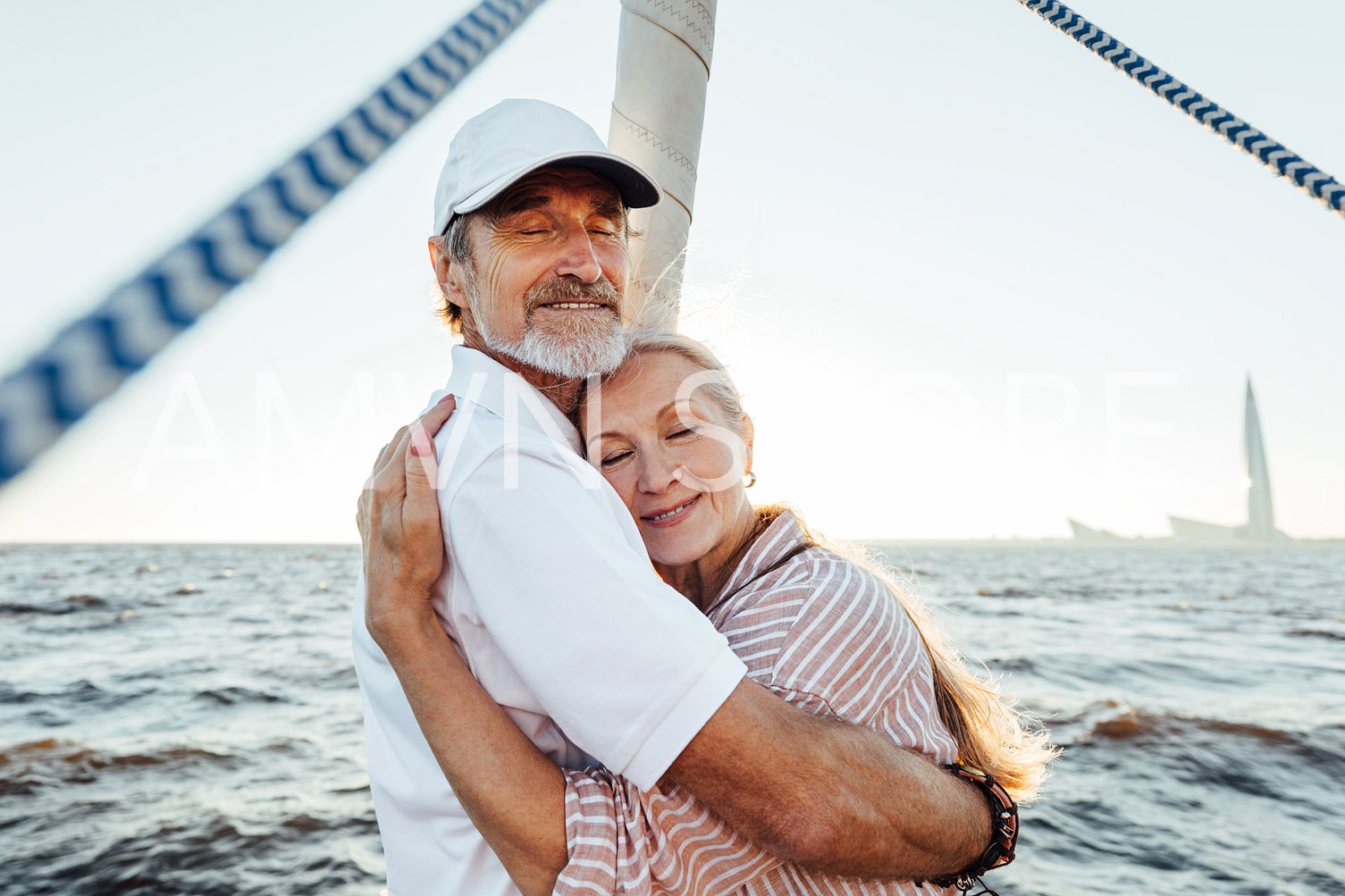 Happy elderly people embracing each other and enjoying a sunset on sailboat. Beautiful mature couple hugging outdoors.	