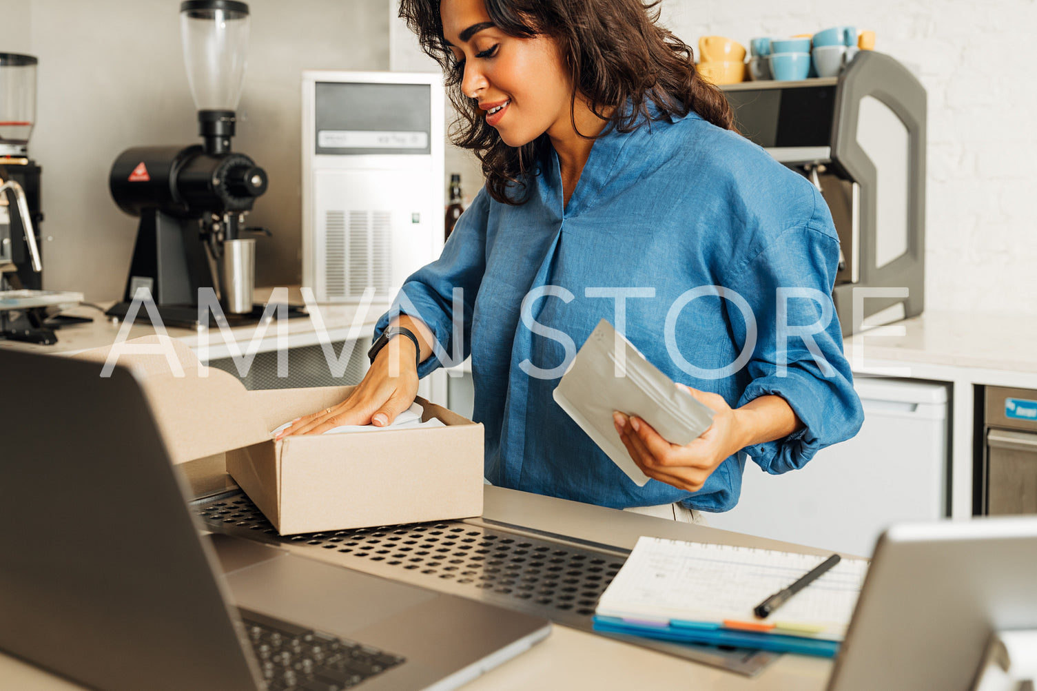 Young business owner puts a pack of coffee into cardboard box for shipment. Coffee shop owner preparing online order.	