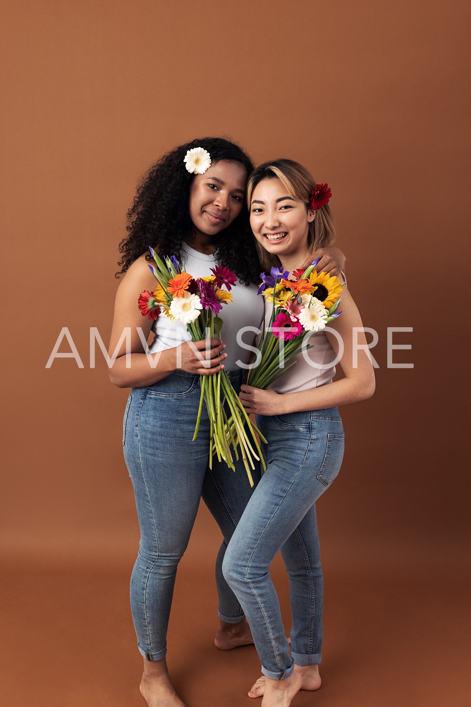 Asian and mixed race women posing against a brown background. Two smiling females with bouquets looking at camera.