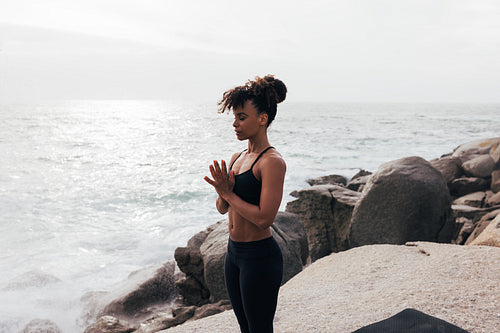 Young woman standing with folded hands at sunset by the ocean