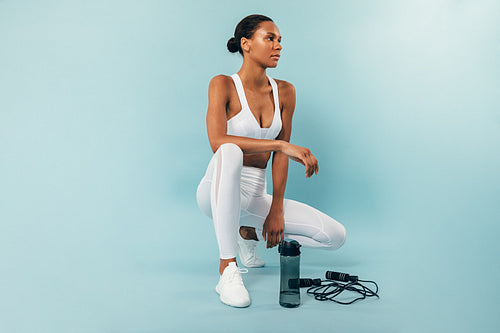 Woman in white sport clothes sitting at a blue background and looking away