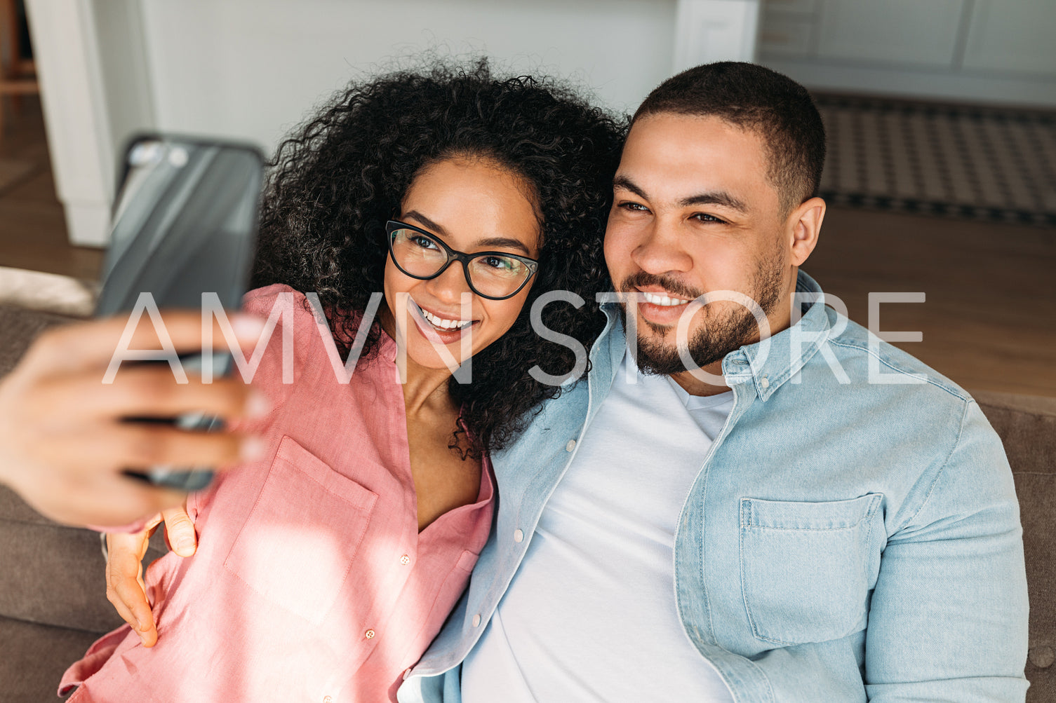 Positive loving couple resting on couch at home and taking selfie on smartphone