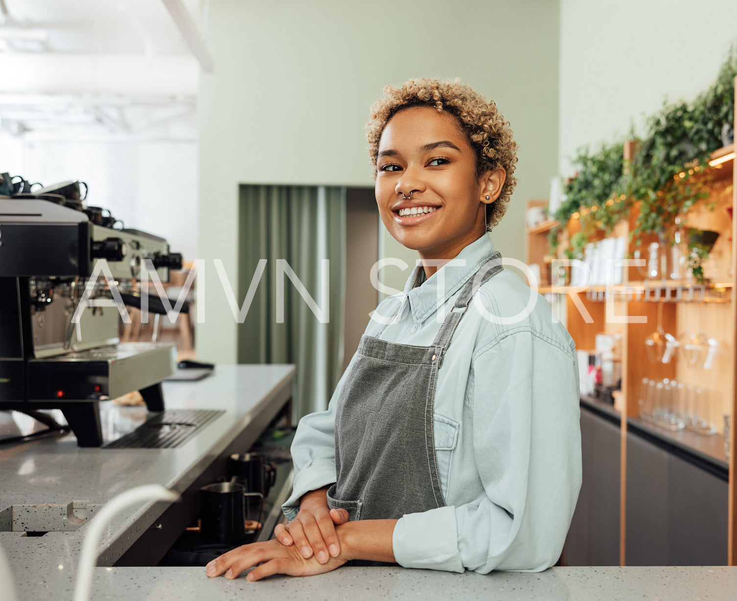 Young smiling barista in an apron leaning counter in a coffee shop. Portrait of a cheerful female bartender.