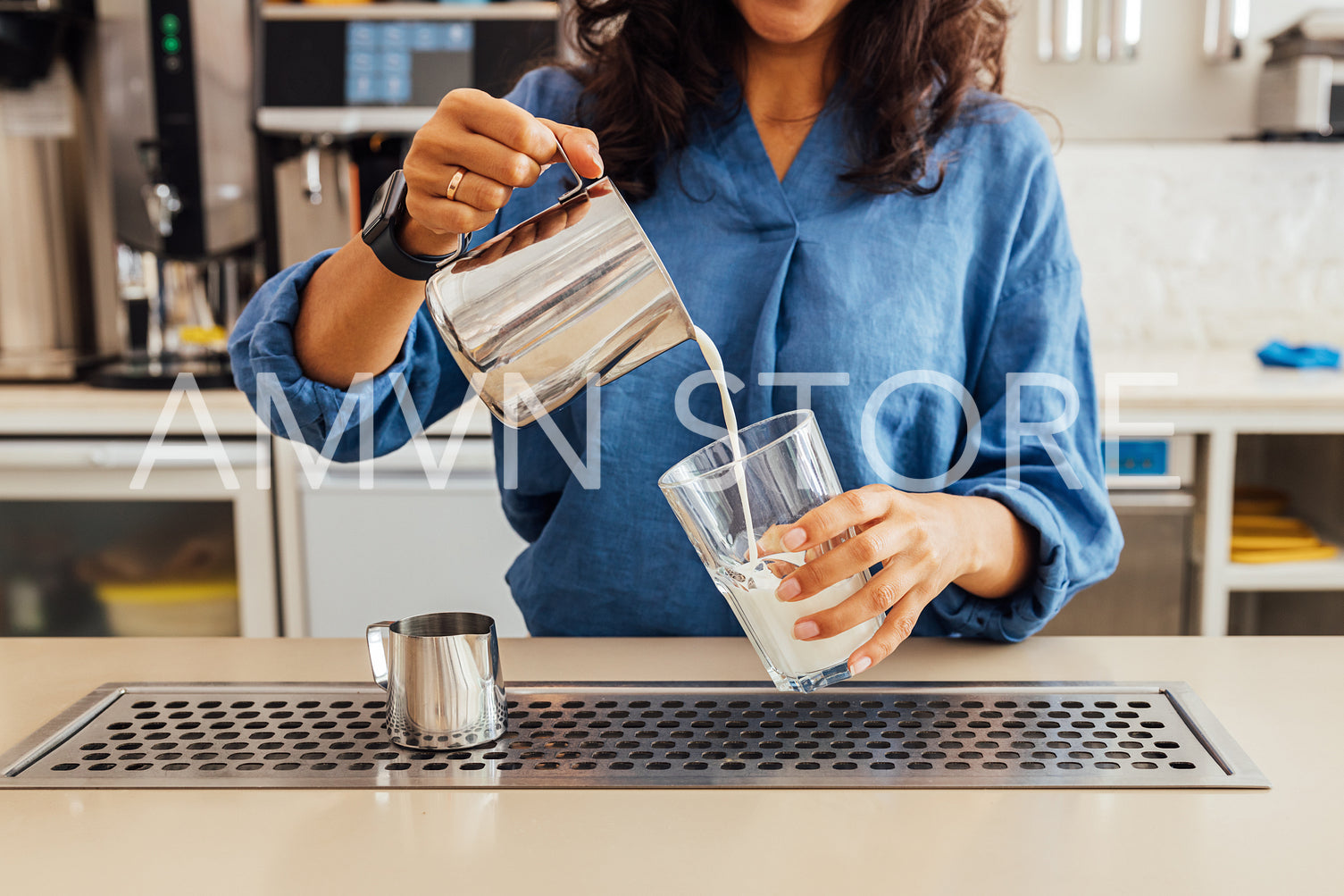 Mid section of a female barista pouring milk from steel frothing pitcher into a glass	