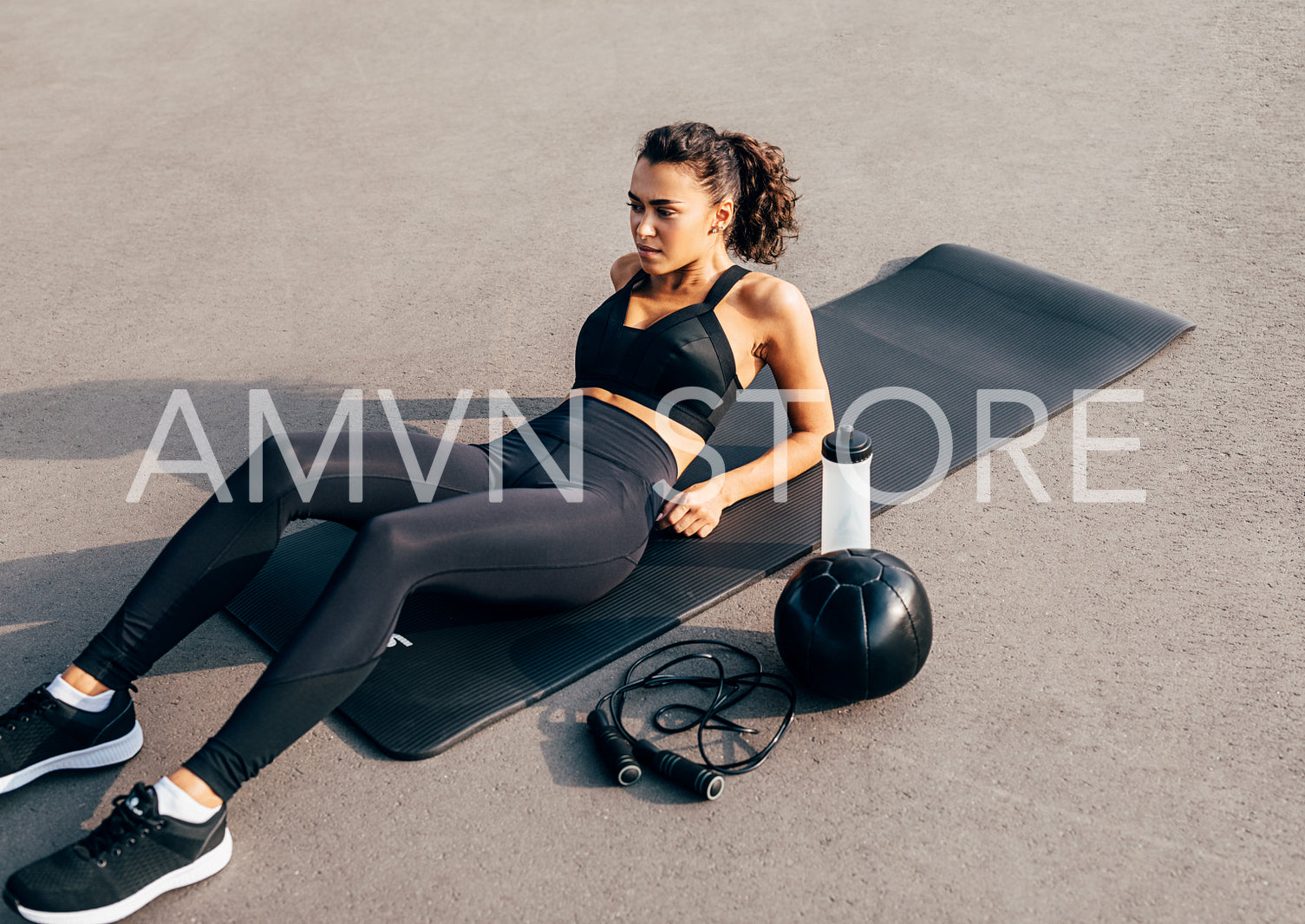 Female in sportswear lying on an exercise mat with a medicine ball, skipping rope and bottle	