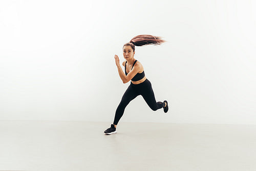 Front view of muscular woman running in studio against white wall